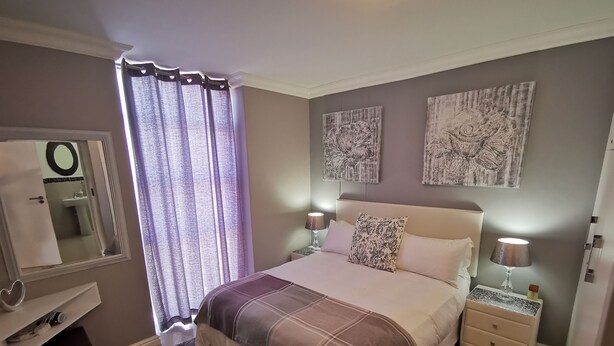 A bedroom with a bed, bedside tables, a nightstand, a mirror, and curtains. - The Sands B32 (Cape Town)