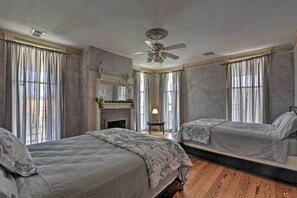 Ein Schlafzimmer mit zwei Betten, einem Deckenventilator, einem Kamin und großen Fenstern mit Vorhängen.