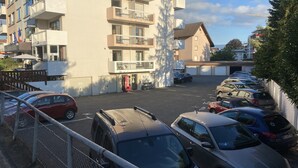 Un espace de stationnement avec plusieurs voitures, un immeuble doté de balcons et un distributeur automatique de Coca-Cola.