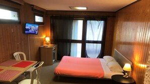 Une chambre d’hôtel avec un lit, un bureau, une chaise, une télévision et une fenêtre avec des rideaux.