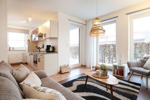A modern apartment with a living room, kitchen, and dining area. It features a large window, a hanging light fixture, and a cozy sofa set.