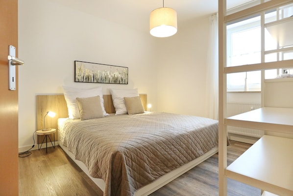 Ein Schlafzimmer mit Bett, Nachttischlampen, einem Bild an der Wand und einem Fenster mit Jalousien.