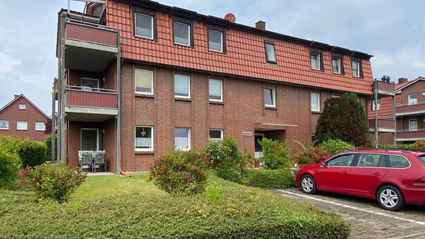 Un edificio residencial de varios pisos con fachada de ladrillo, balcones y un coche rojo estacionado en la entrada.