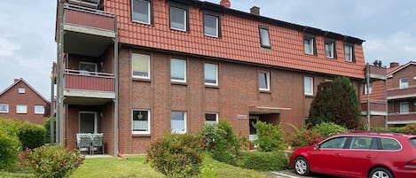 Kerrostalo, jossa on tiiliverhous, parvekkeet ja punainen auto pysäköitynä ajotielle.
