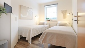 Una habitación con dos camas, un ventanal grande, una planta y un cuadro.
