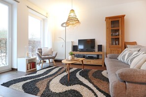 Ein Wohnzimmer mit Sofa, Sessel, Fernseher, Holzschrank und einem gemusterten Teppich.