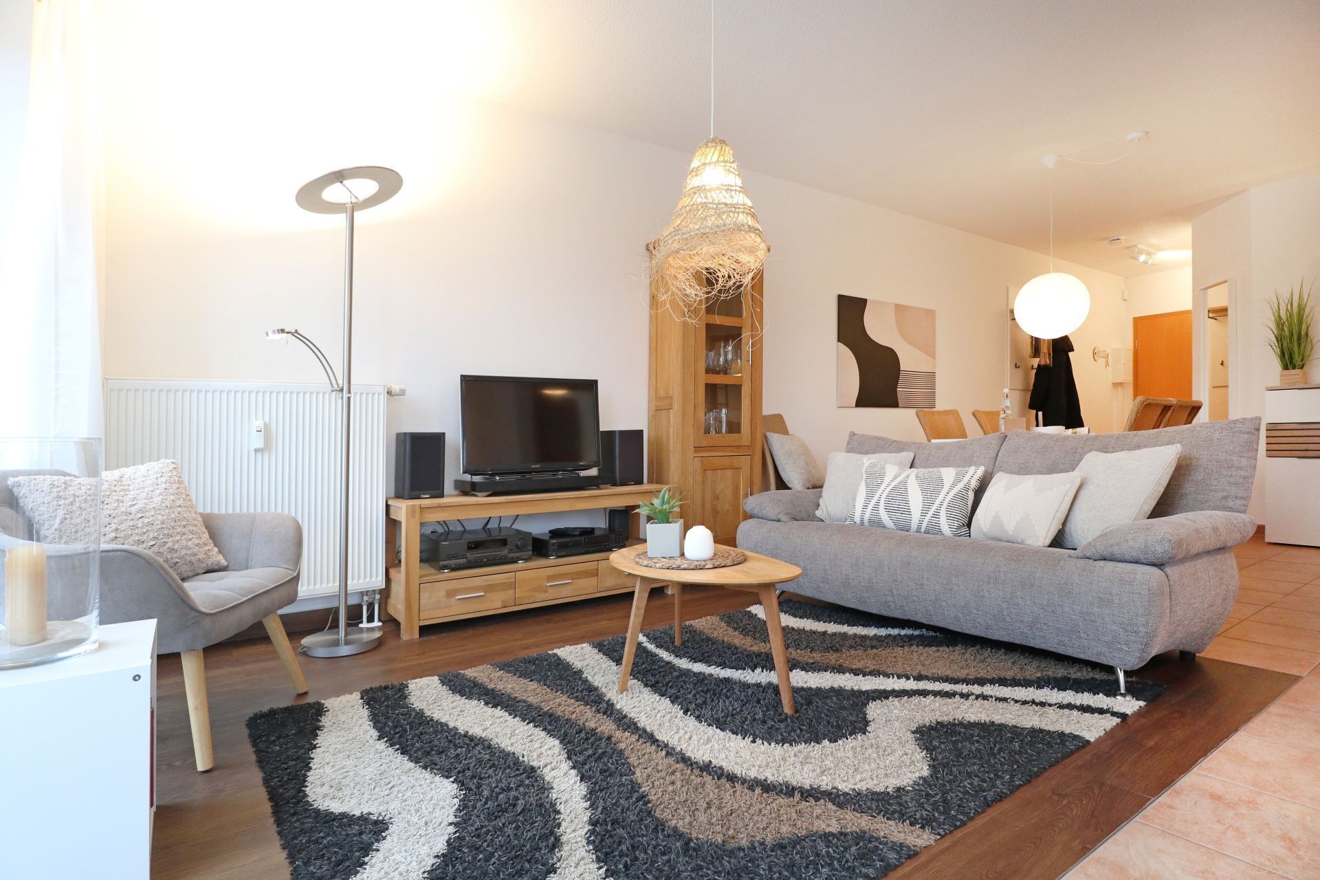 Un soggiorno moderno con un divano grigio, un mobile in legno, una TV e un originale lampadario a sospensione.