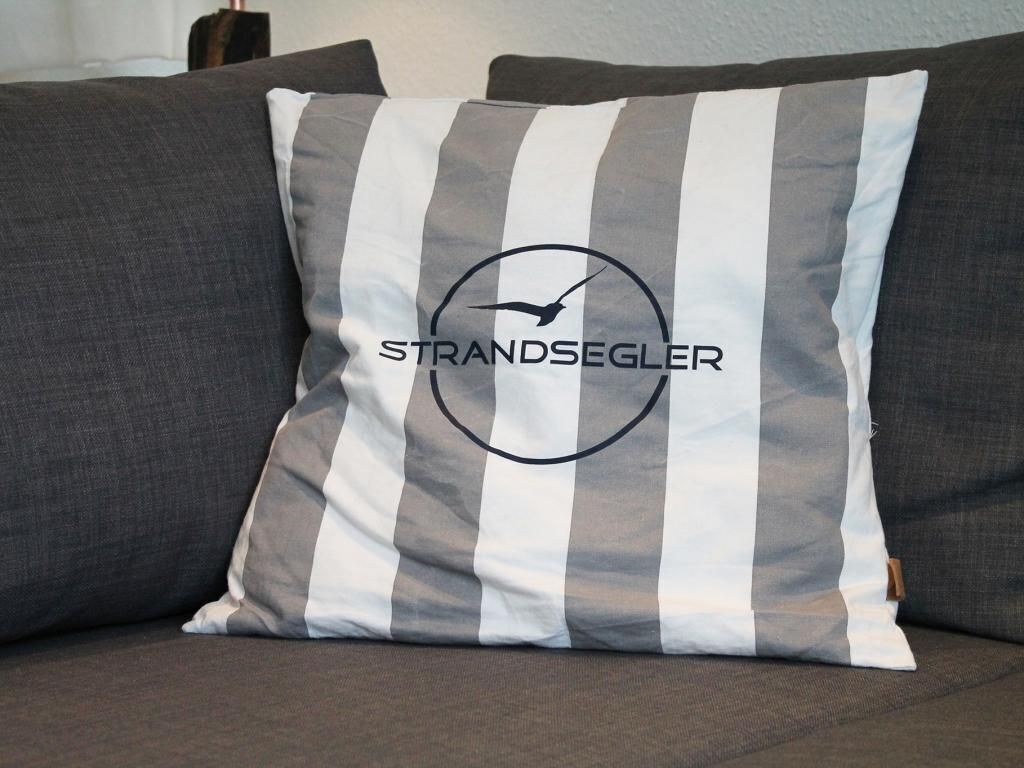 A pillow with a striped pattern and the text "STRANDEGLER" on a couch.