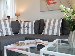 A modern living room with a grey sofa, striped cushions, and a glass coffee table with magazines. - Beach sailor, Germany (Dassow)