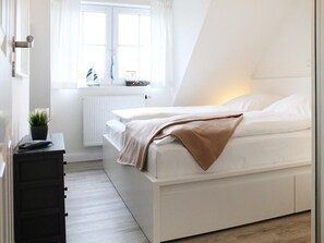 Quarto moderno com cama, cômoda, radiador e janela com cortinas.