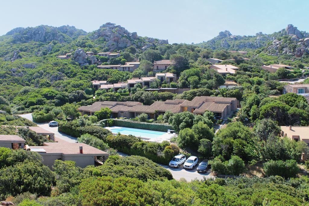Zona residencial con casas, piscina y área de estacionamiento, rodeada de vegetación y colinas.