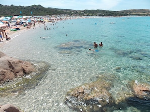 A beach with clear water, people swimming, and umbrellas.