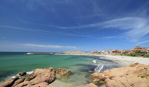 A coastal town with a rocky shoreline, clear turquoise waters, and buildings with Mediterranean architecture.
