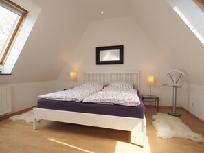 A bedroom with a bed, a mirror, a radiator, a floor lamp, and a fur rug. - Beach view, Germany (Ostseebad Boltenhagen)