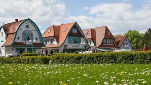 Een rij traditionele gebouwen in Europese stijl met schuine daken, een centraal bordje dat een restaurant en café aangeeft, en een verzorgde tuin op de voorgrond.