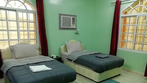 Habitación con dos camas, una ventana con cortinas, aire acondicionado de pared y piso de baldosas.
