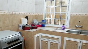 Una cocina con estufa, horno y pileta. Hay platos, tazas y una caja en la encimera.