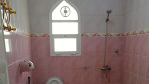 Un baño pequeño con azulejos rosas, un inodoro, una ducha, una ventana y un tapete azul.
