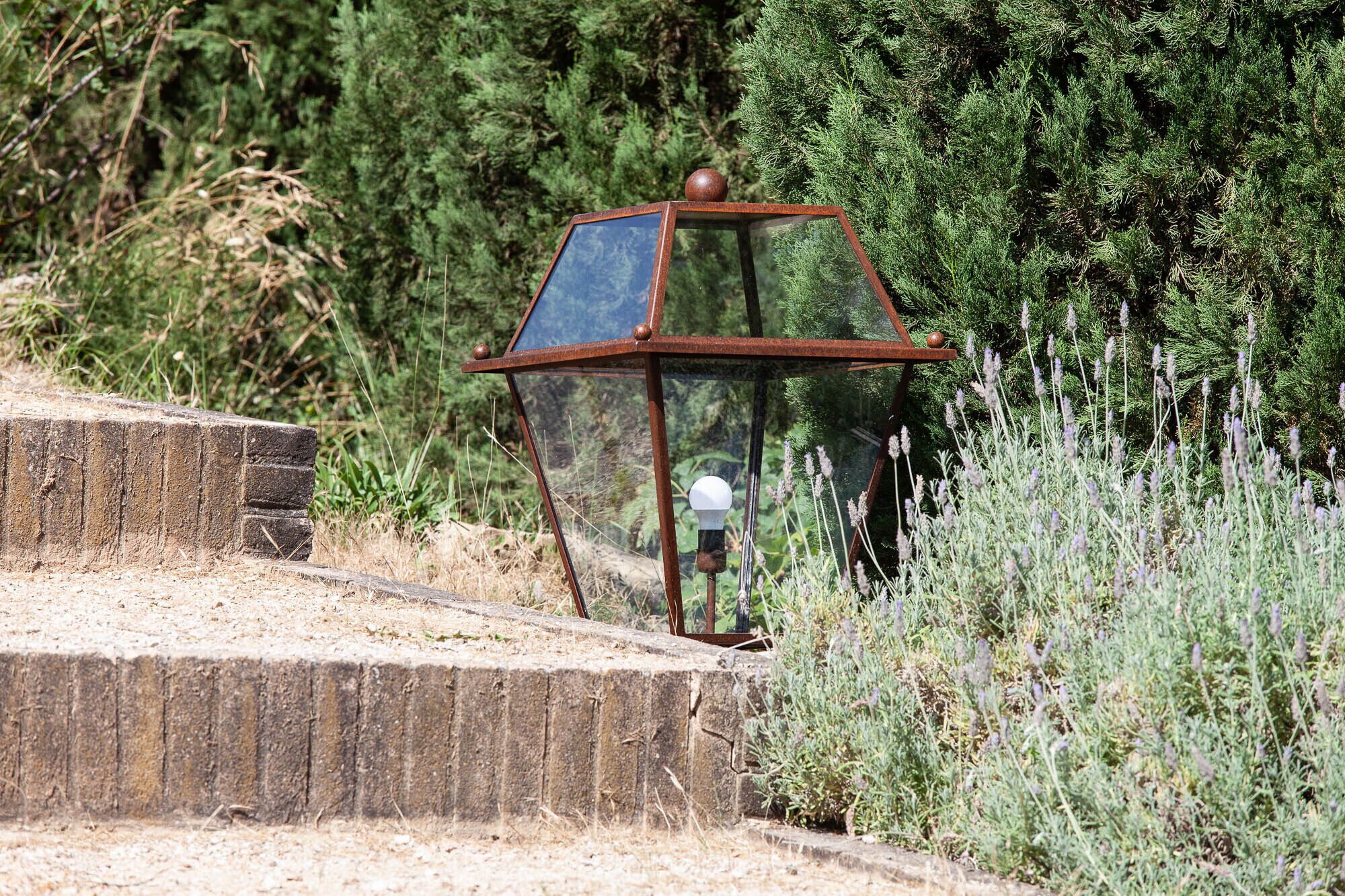 A rustic metal lantern with a glass enclosure, situated on a stone ledge surrounded by greenery.