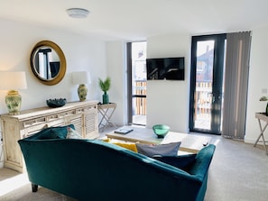 Uma sala de estar com um sofá verde-água, um armário de madeira, uma televisão e uma janela grande com cortinas.