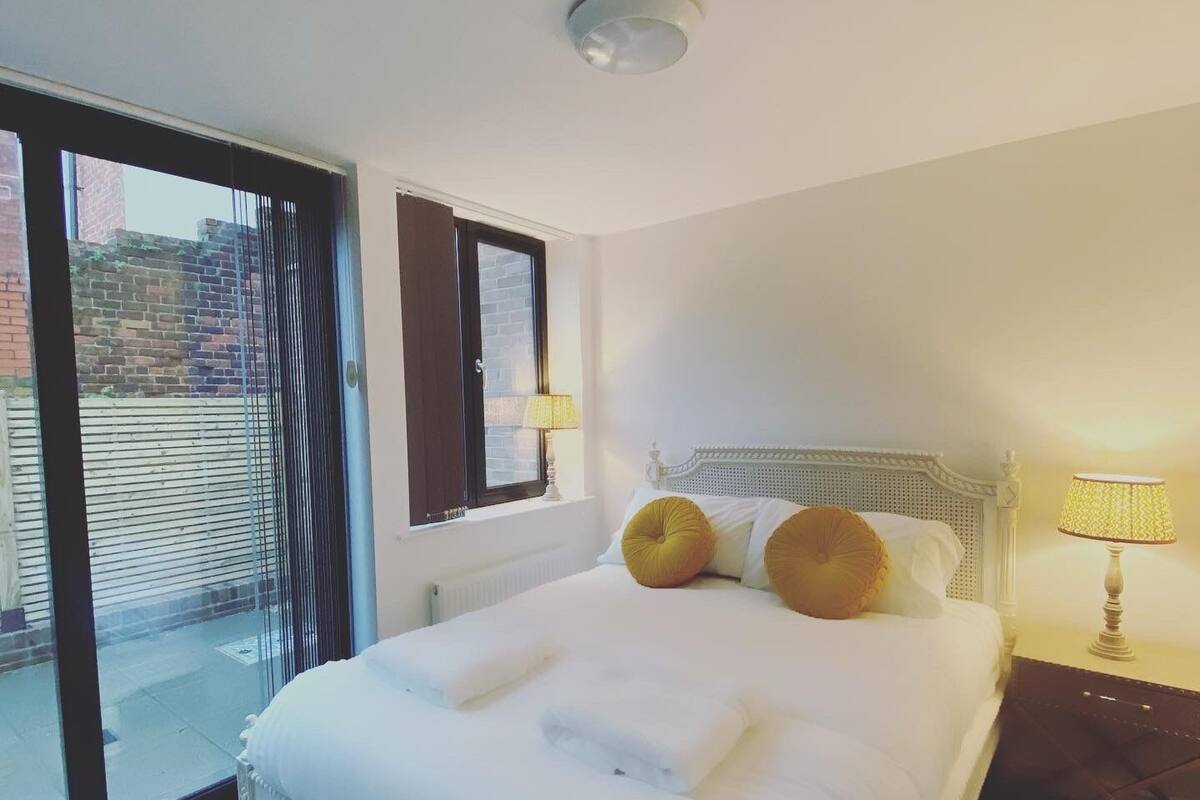 A hotel room with a large bed, a window with blinds, a lamp, and a view of the outside.