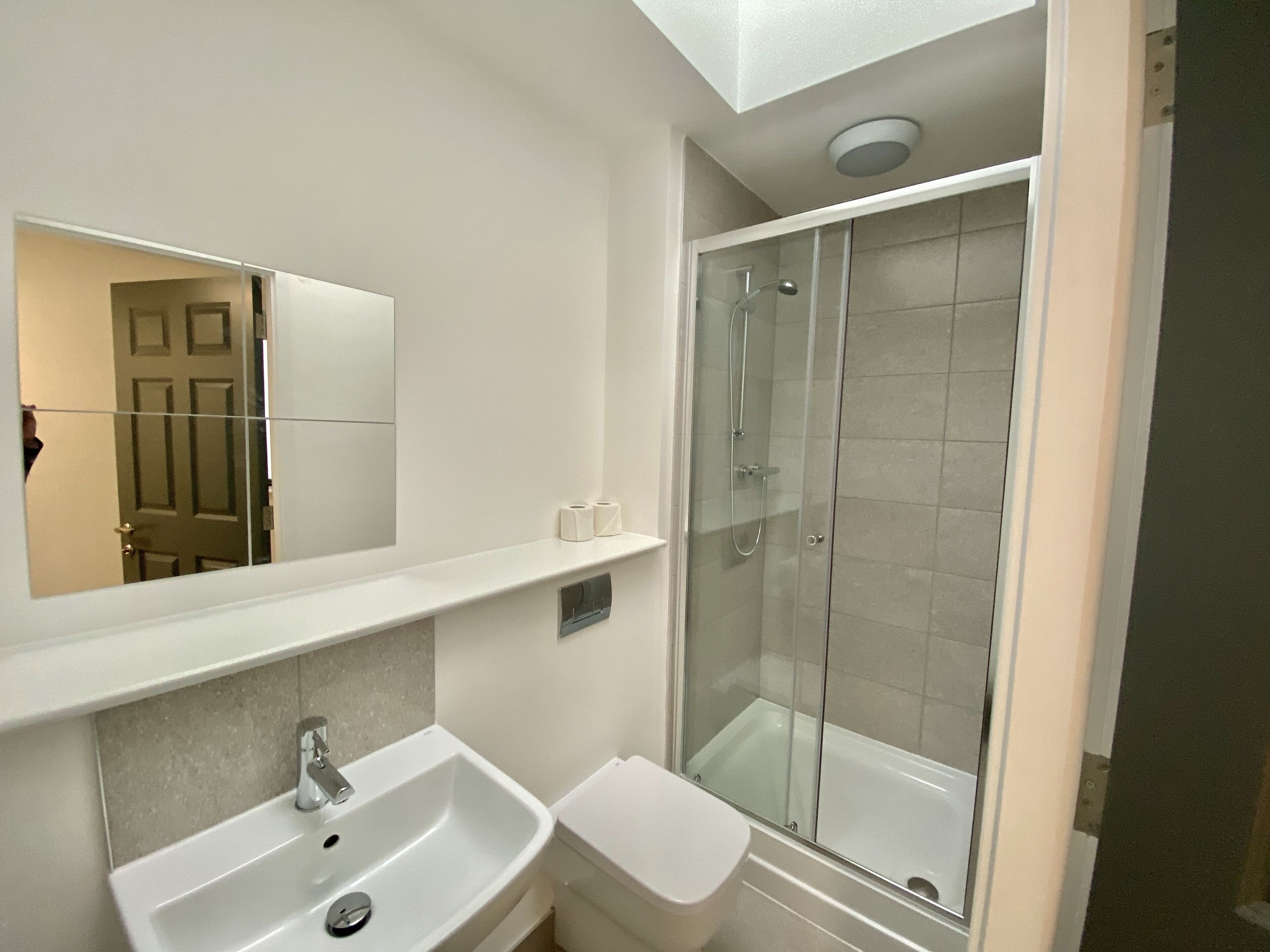 A modern bathroom with a glass-enclosed shower, a white sink, and a mirror above the sink.