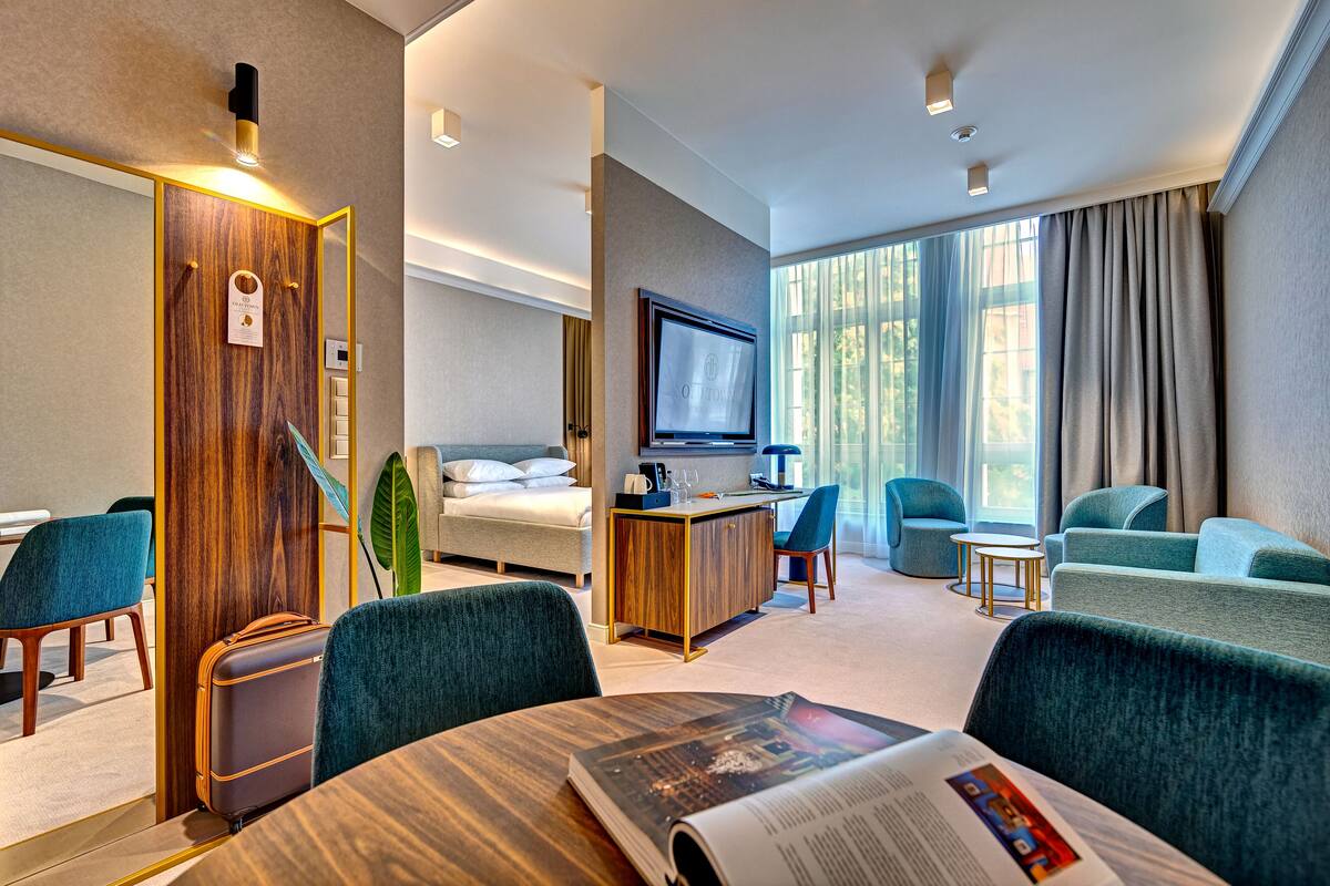 A modern hotel room with a bed, a desk, a TV, and seating areas.