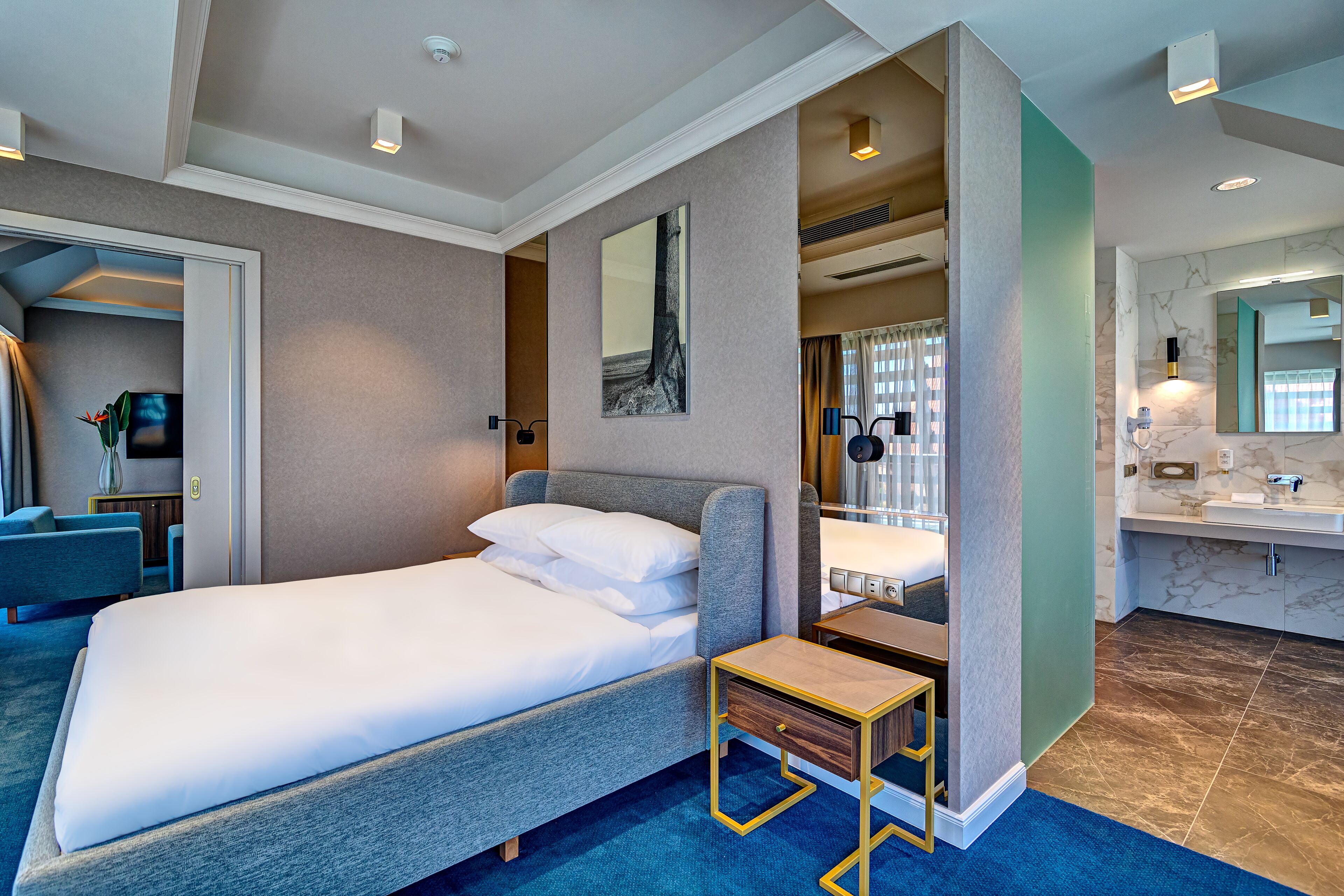 Una habitación de hotel con cama, mesita de noche y baño con lavamanos y espejo.
