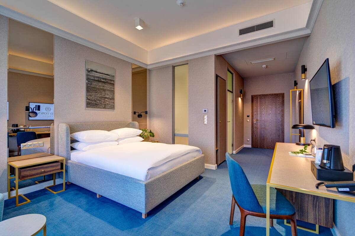 A hotel room with a bed, desk, chair, and a television.