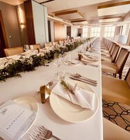 Een lange feesttafel gedekt voor een formeel evenement, met witte tafelkleden, net geordende borden, glazen en bestek.