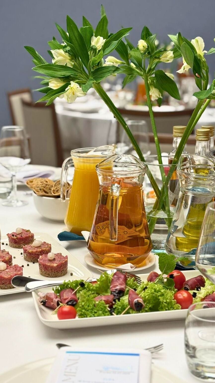 Una mesa dispuesta con diversos alimentos, incluyendo una jarra de jugo de naranja, una botella de aceite de oliva y un plato de aperitivos.