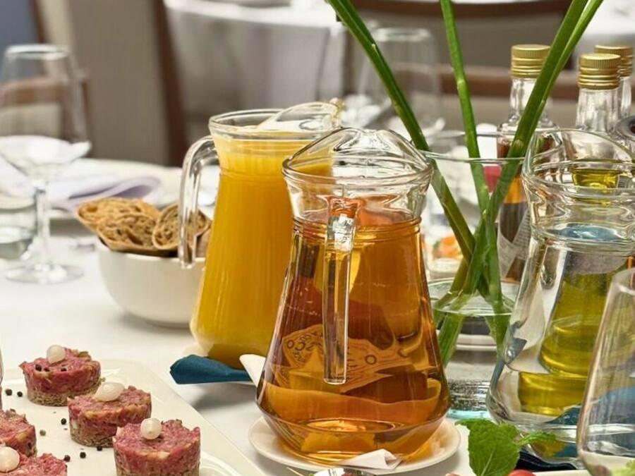 Una mesa dispuesta con diversos alimentos, incluyendo una jarra de jugo de naranja, una botella de aceite de oliva y un plato de aperitivos.