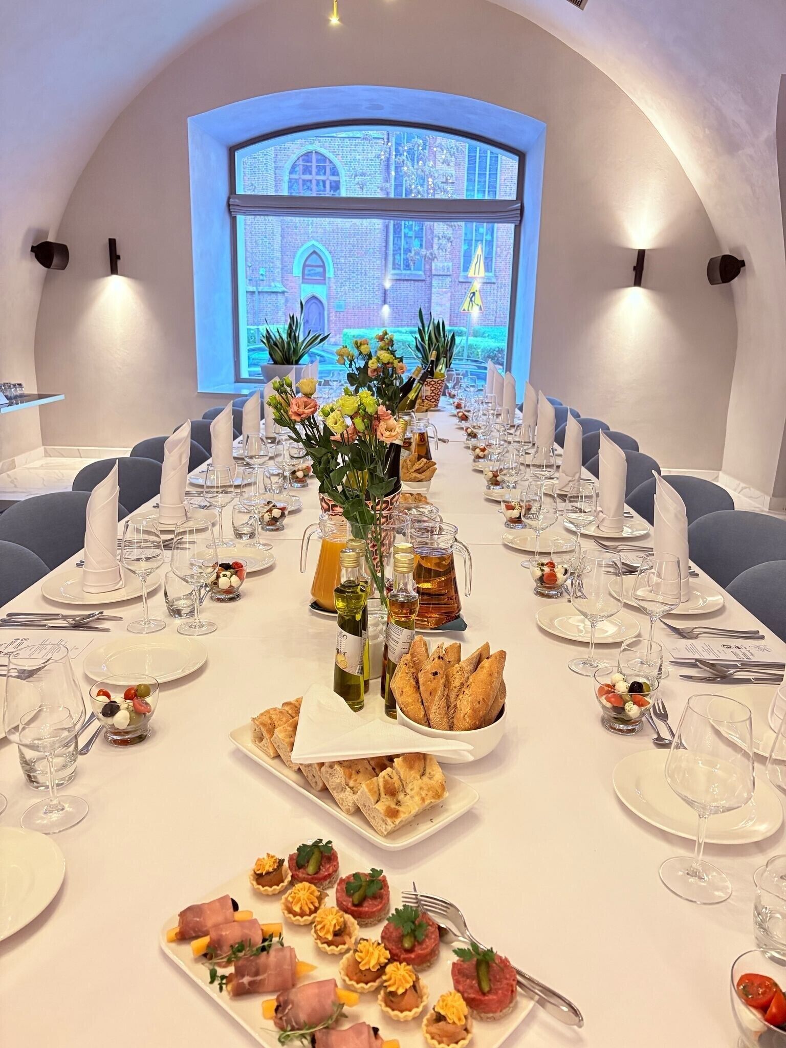 Une longue table à manger, dressée pour un repas formel composé de plusieurs plats, notamment des hors-d'œuvre, des plats principaux et des desserts.