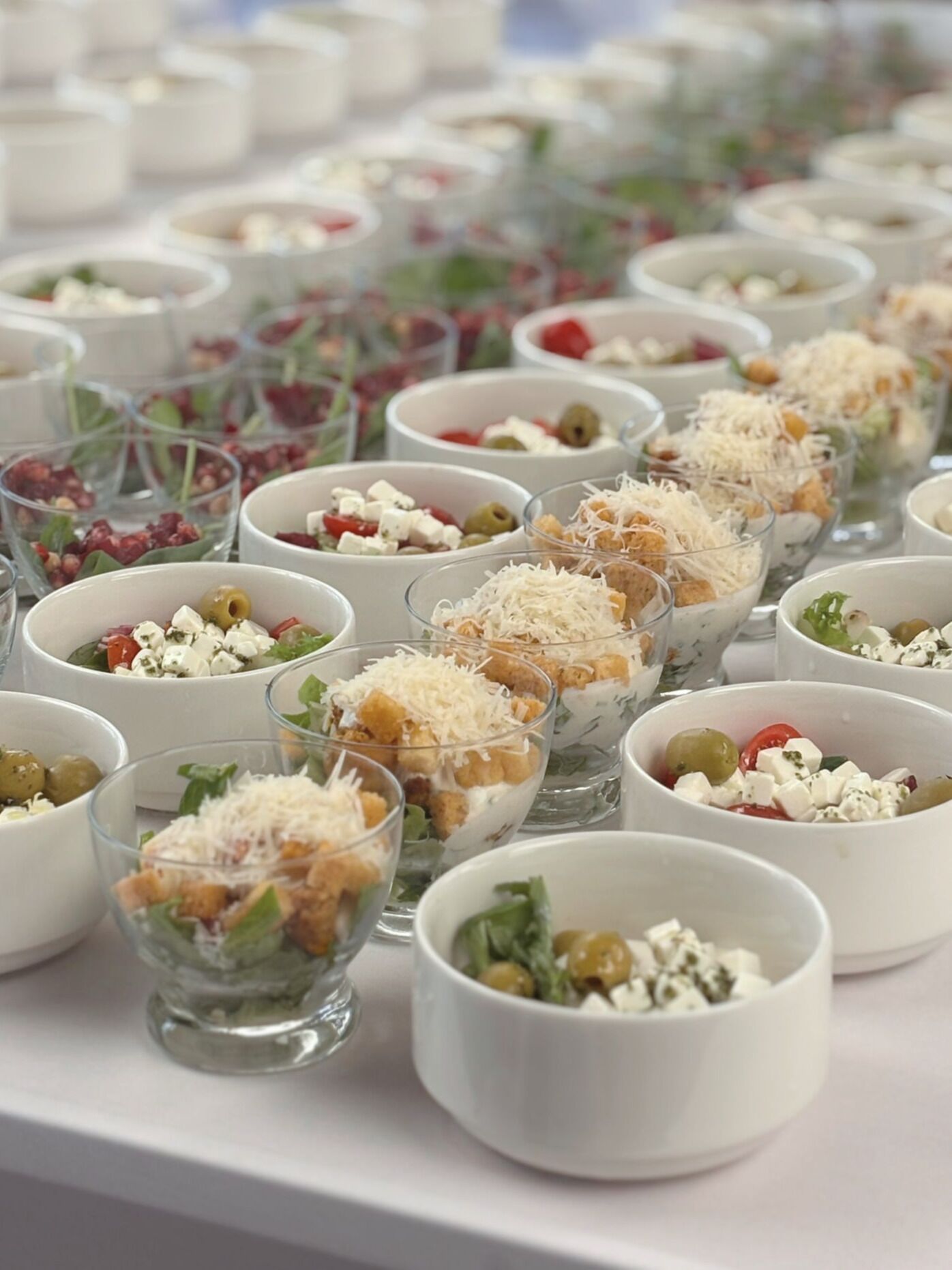 Diversas pequenas tigelas de vidro com diferentes tipos de comida, provavelmente uma seleção de buffet ou aperitivos.