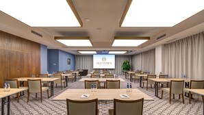 A conference room with multiple tables, chairs, and a large screen displaying the hotel name. - Haston Old Town (Wroclaw)
