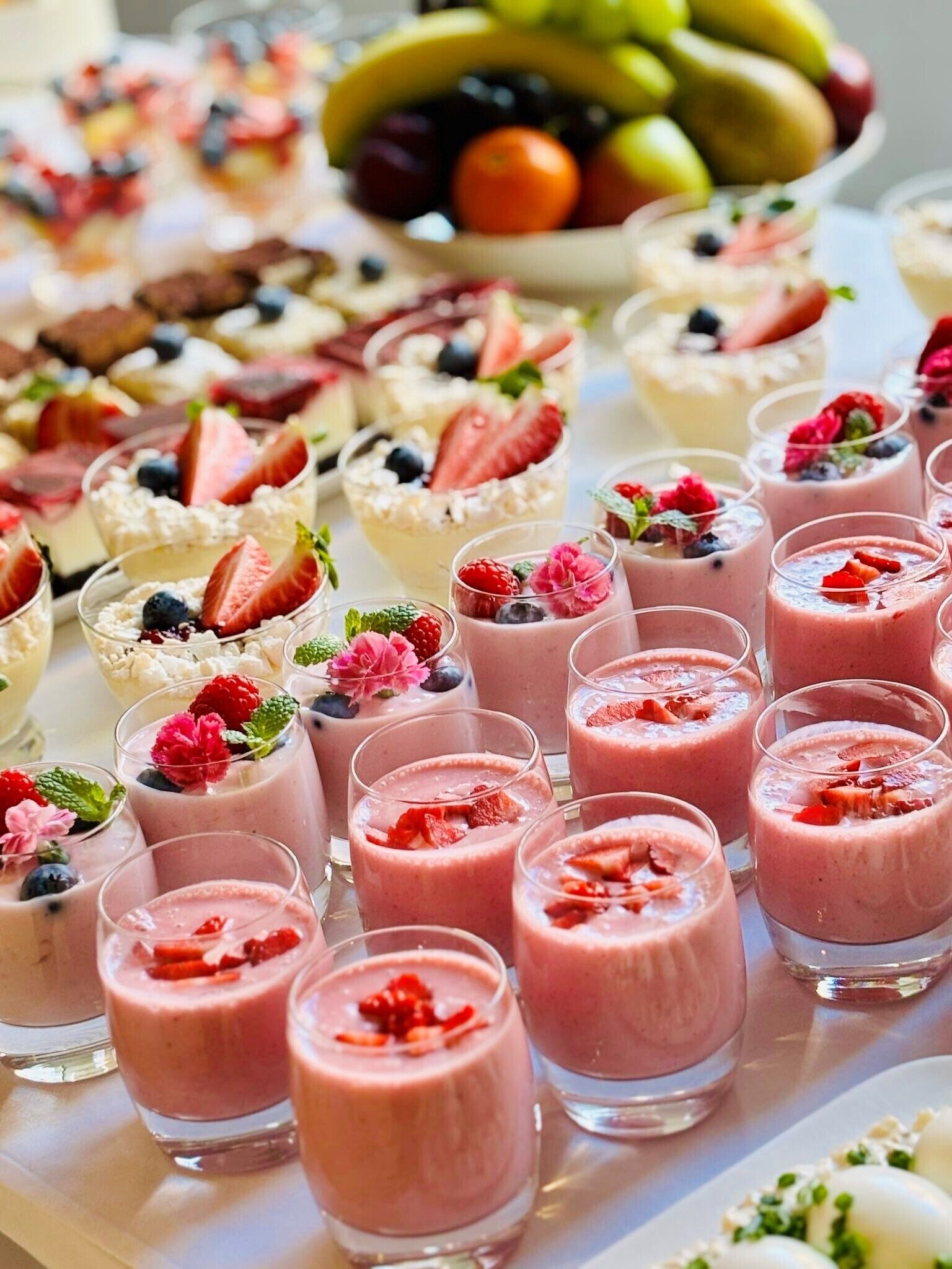 A variety of fruit-based desserts and beverages, including smoothies and yogurt parfaits, arranged on a table.