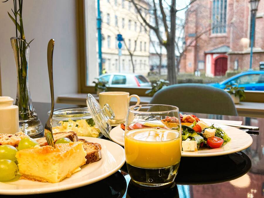 A breakfast table with plates of food, a glass of orange juice, and a vase with flowers.