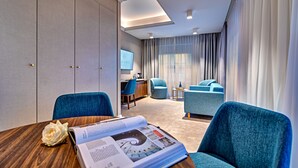 A modern hotel room with a wooden dining table, a magazine, a blue chair, a sofa, and a TV on the wall. - Haston Old Town (Wroclaw)