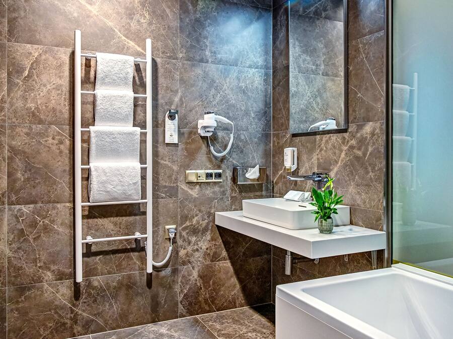 A modern bathroom with a marble-tiled wall, a white sink, a mirror, a towel rack, and a shower.