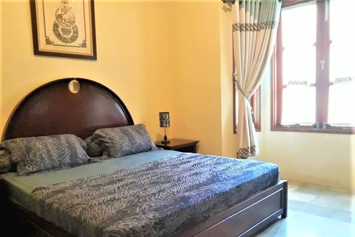 A bedroom with a bed, a nightstand, a framed picture on the wall, and a window with curtains.