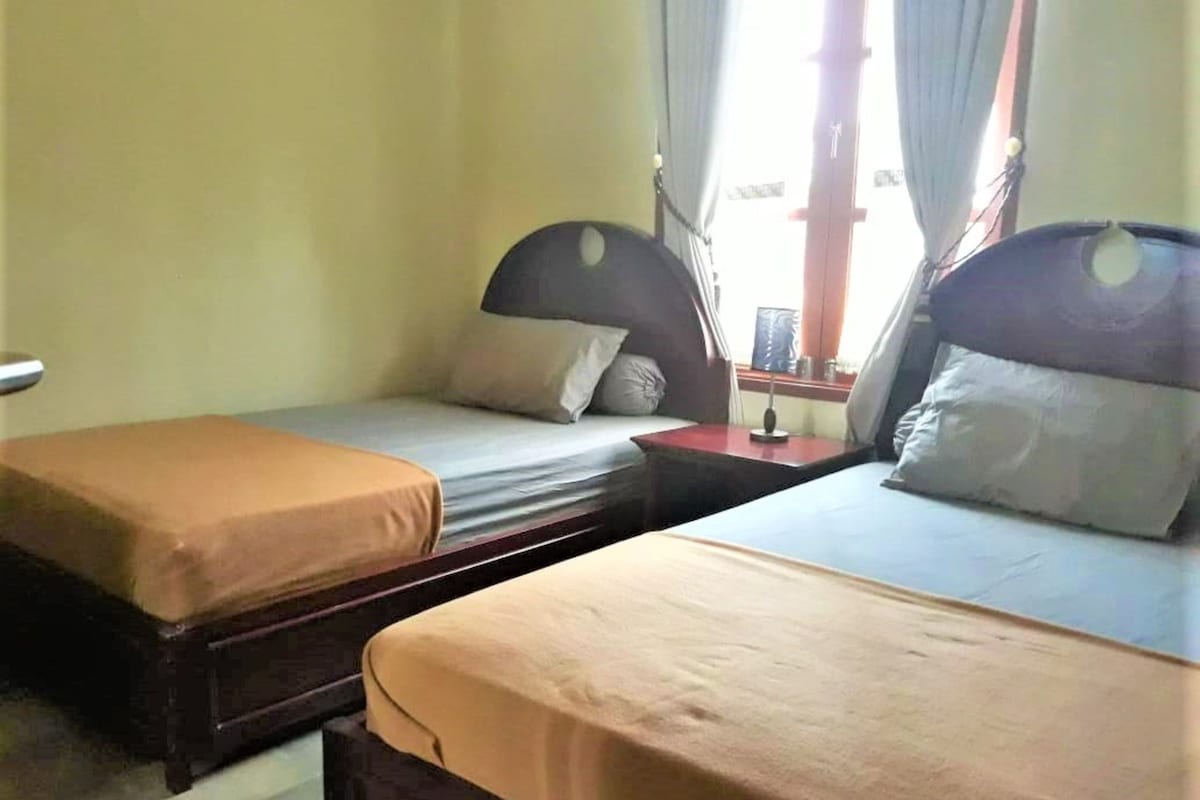 Ein Hotelzimmer mit zwei Einzelbetten, einem kleinen Tisch und einem Fenster mit Vorhängen.