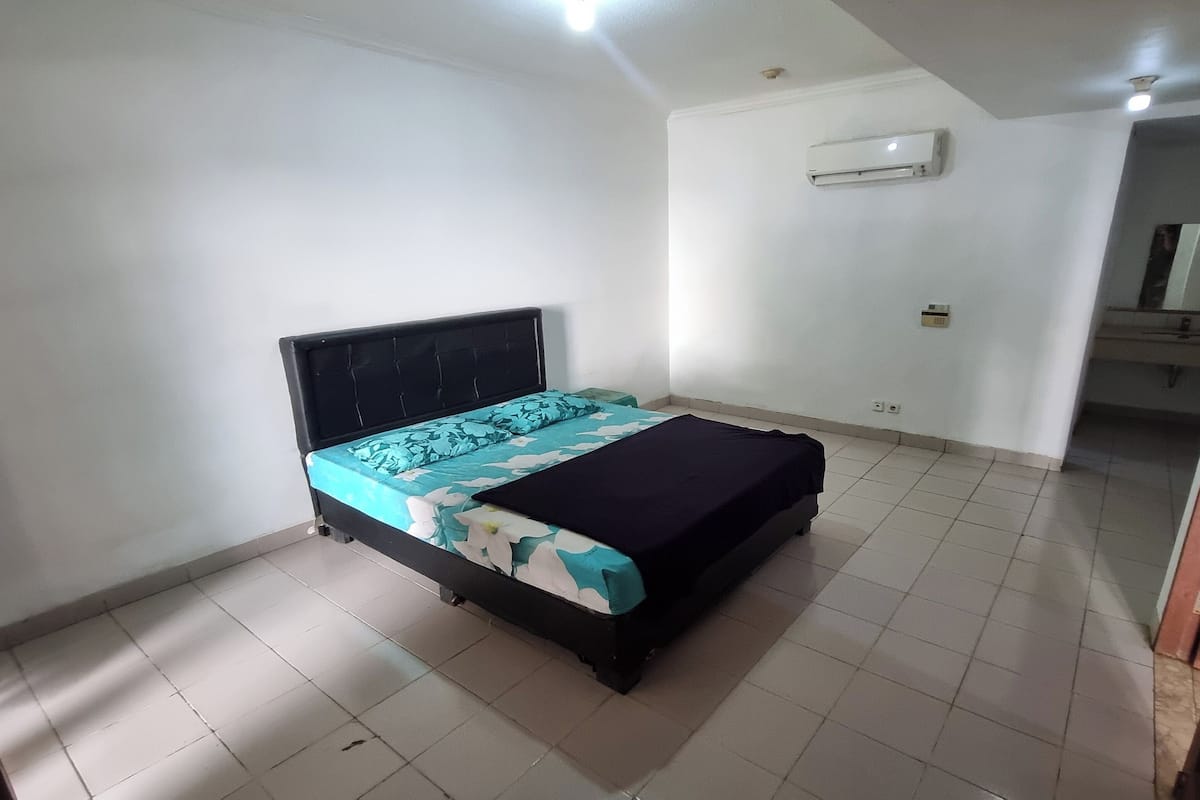 A bedroom with a bed, white walls, an air conditioning unit, and a visible door.