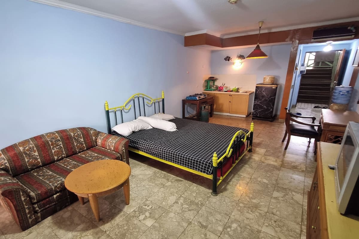 A bedroom with a bed, a sofa, a small table, a desk, and a television.