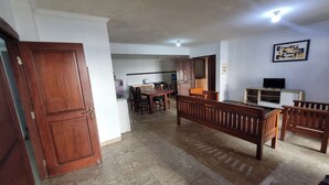 Una sala de estar con un banco de madera, un televisor y una cocina al fondo.