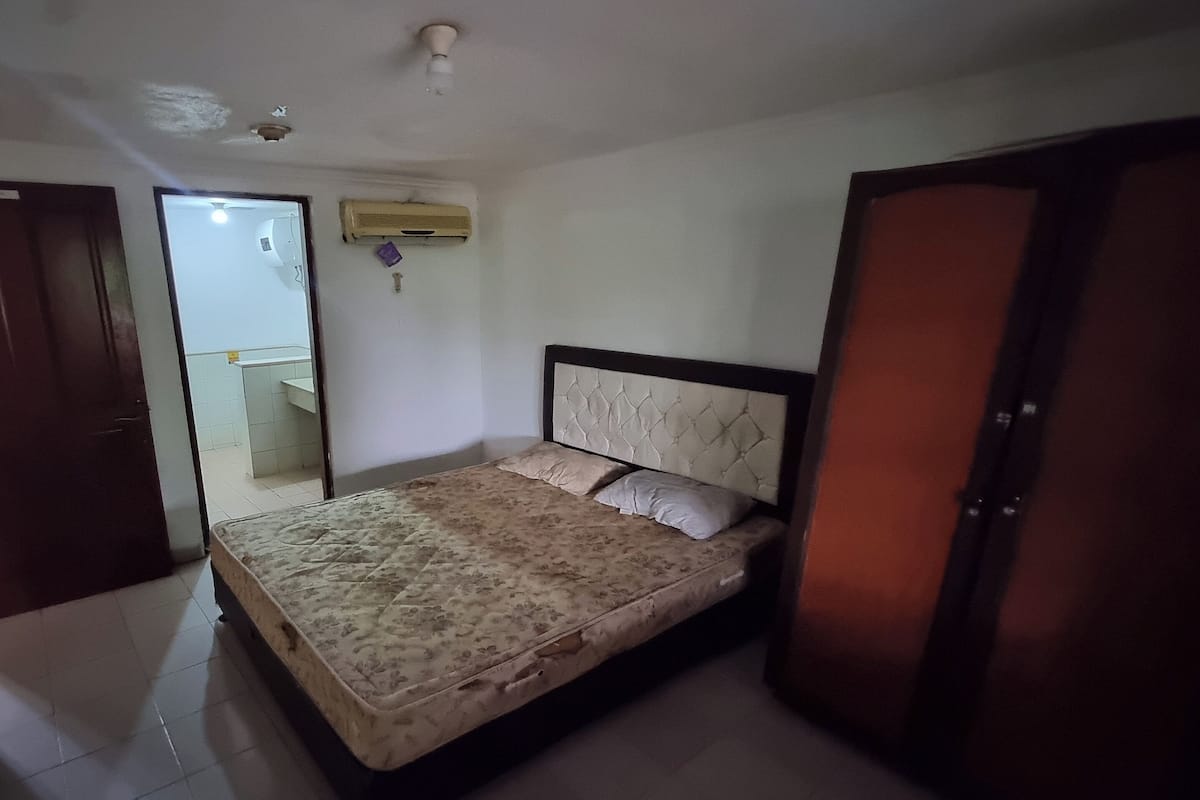 A bedroom with a bed, a door, and an air conditioning unit on the wall.