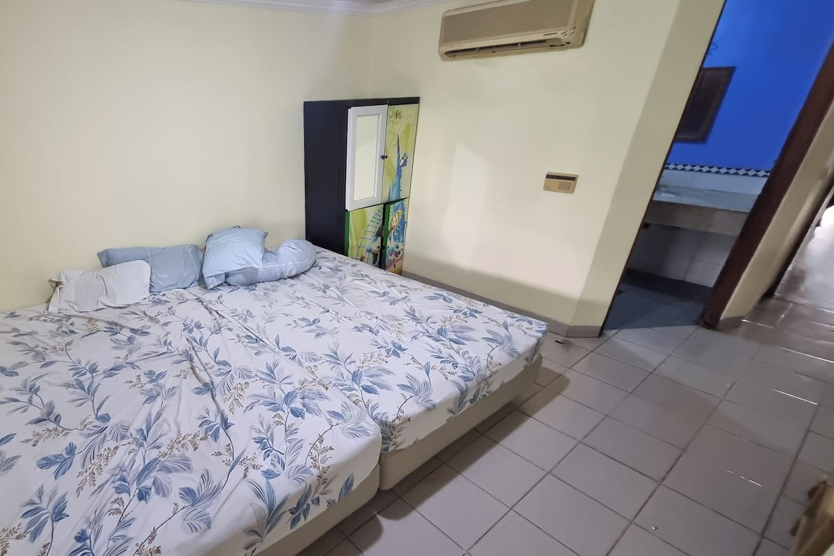 A bedroom with a bed, pillows, a wardrobe, and a door leading to another room.