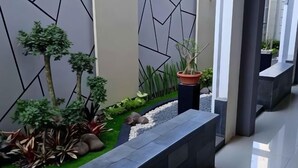 A modern indoor garden with artificial trees, a variety of plants, and a stone pathway. - Alzara Hotel Syariah (Wonosari)
