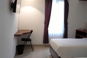 A bedroom with a bed, a desk, a chair, a small trash bin, and a window with curtains. - Alzara Hotel Syariah (Wonosari)
