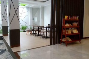 A modern interior with a dining area, a bookshelf, and a view of the outdoors. - Alzara Hotel Syariah (Wonosari)