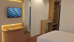 A hotel room with a TV mounted on the wall, wooden furniture, and a bed. - Alzara Hotel Syariah (Wonosari)